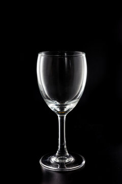 An empty transparent stemmed wine glass, placed against a solid black studio background, with no liquid inside.