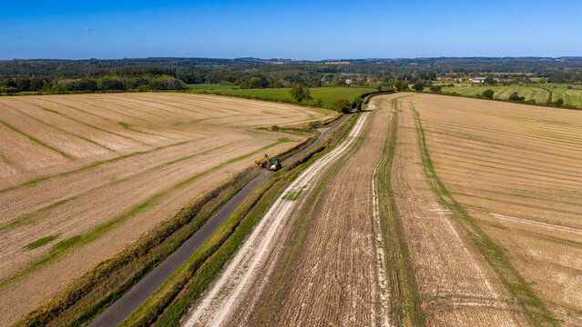 Aerial view of a tractor trimming hedges along a country road through harvested fields at Pepperbox Hill in Salisbury, England, United Kingdom.
