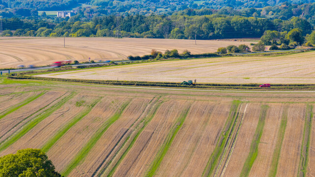 Aerial view of the agricultural landscape at National Trust - Pepperbox Hill, featuring harvested fields, a road with vehicles, and green trees in Salisbury, England, United Kingdom.