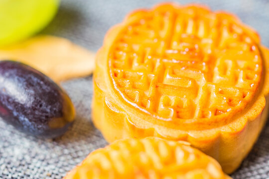 Close-up view of glossy baked traditional mooncakes with fresh grapes on a textured gray surface.