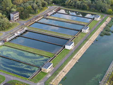 Aerial view of a water treatment plant with rectangular sedimentation tanks and filtration basins surrounded by lush greenery in Poland.