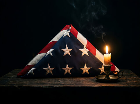 Folded american flag beside a lit candle on wooden table for veteran day with memorial day