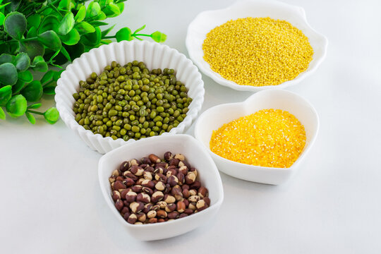 A still life display of four different types of uncooked grains and legumes, each in a separate white bowl, arranged on a plain white surface.