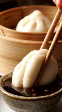 Wooden chopsticks dipping a soft white steamed bao bun into a small bowl of hoisin sauce