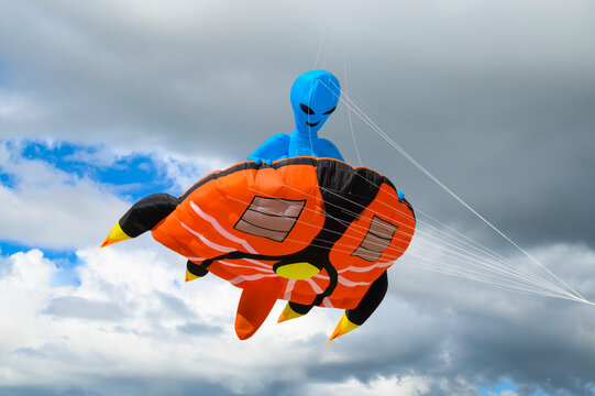 Ōtaki Beach, Wellington, New Zealand, March 14 2-26. A single kite in the form of an alien riding on a flat spaceship against a cloudy but fine summers day. The strings can be seen as the kite flies