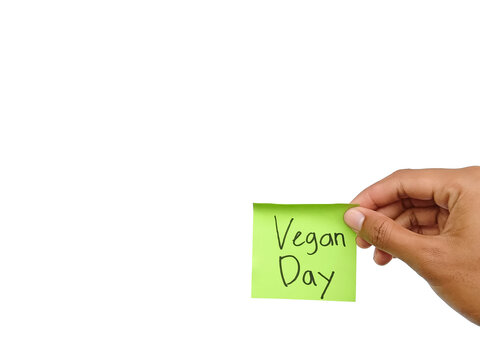 Close up hand holding a green sticky note with handwritten text Vegan Day isolated on a clean white background. Conceptual photo for world vegan day celebration, vegetarian diet, and healthy lifestyle