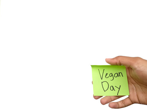 Close up hand holding a green sticky note with handwritten text Vegan Day isolated on a clean white background. Conceptual photo for world vegan day celebration, vegetarian diet, and healthy lifestyle