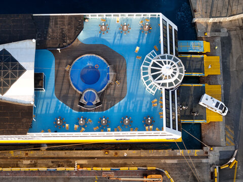 Aerial view of the deck of a ferry to Corsica featuring a swimming pool, sun loungers, and a glass dome structure docked at the port in Vado Ligure, Liguria, Italy.
