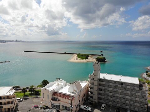 Aerial view of Arah Beach featuring a white sandy beach, emerald-green sea, a small island, and a coastal promenade in Chatan, Okinawa, Japan.