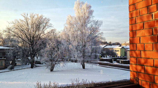 Aerial view of a snow-covered park with frost-laden trees and a red brick wall in the foreground in Latvija.