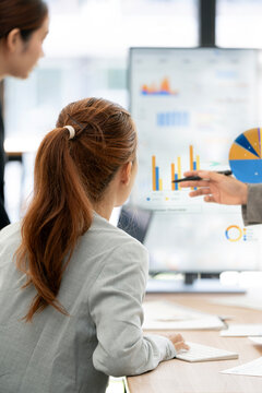Asian Businesswoman Looking at Monitor and Discussing Financial Data in Vertical Framing