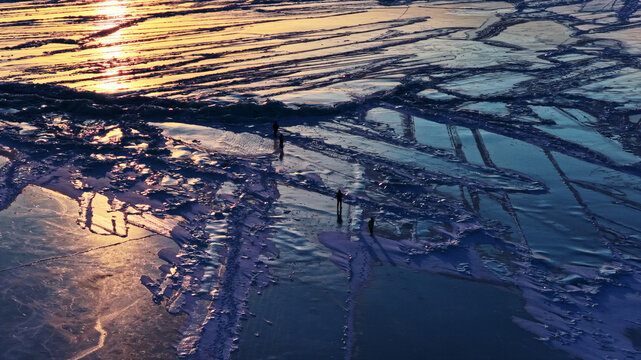 Aerial view of people walking on the cracked ice of a frozen lake during golden hour in Latvia.