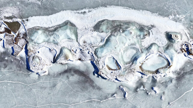 Aerial view of frozen lake with intricate ice cracks, snow-covered patches, and varying textures of ice in Latvia.