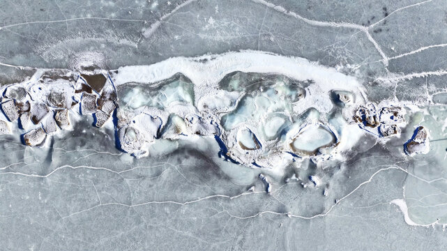 Aerial view of frozen ice surface with intricate cracks and textures on a lake in Latvija.