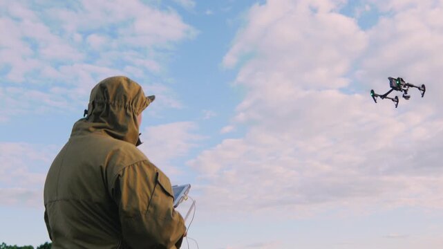 Unmanned aerial vehicle operator controls professional drone while flying over green field.