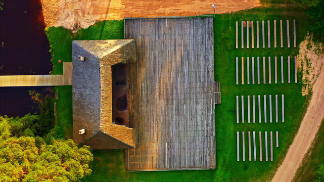 Aerial view of an outdoor wooden stage and rows of benches set in a grassy park near a river in Latvia.