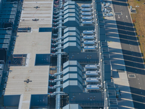 Aerial view of a modern datacenter facility featuring rows of industrial cooling units and ventilation systems on the roof, set against an asphalt road in The Netherlands.