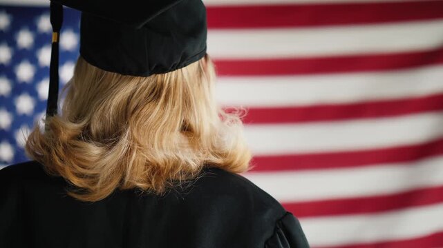 Happy female graduate student holding diploma scroll against American flag background.