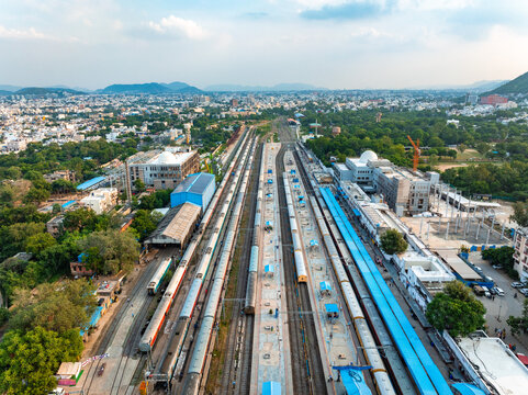 Aerial view of Udaipur Railway Station with multiple train tracks, passenger platforms, blue-roofed structures, and surrounding urban landscape in Udaipur, Rajasthan, India.