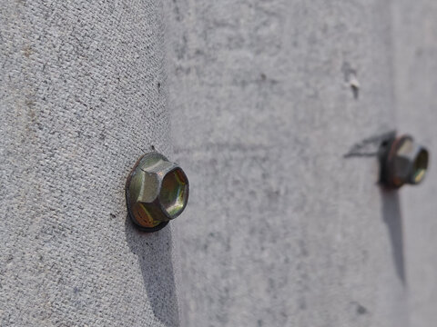 a zinc-plated hex bolt and washer securely fastened to a rough, textured concrete utility power pole. Features a shallow depth of field with a secondary bolt softly blurred in the background bokeh