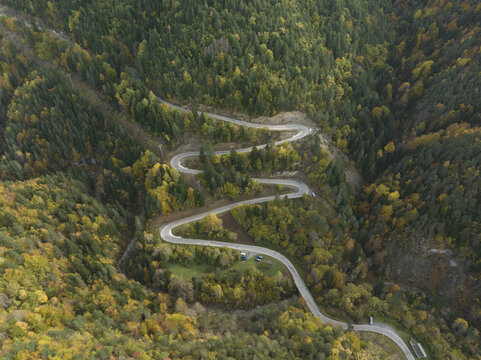 Aerial view of a winding mountain road through the dense autumn forest of the Pyrenees in Spain.
