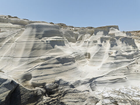 Aerial view of the white volcanic rock formations of Sarakiniko beach with smooth textures and deep shadows under a clear blue sky in Milos, Greece.