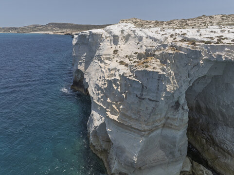 Aerial view of the white volcanic rock formations of Sarakiniko beach meeting the turquoise Aegean Sea in Milos, Greece.