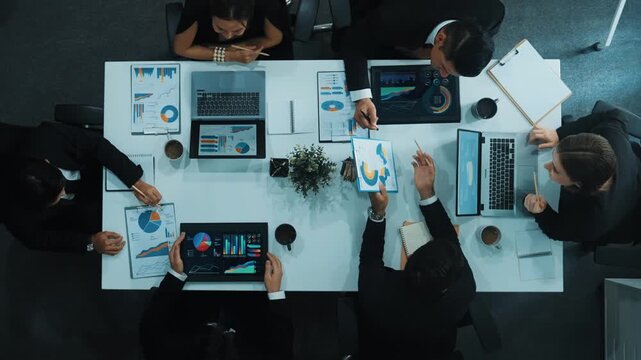 Top down aerial view of business people discussing about financial strategy on table with document and tablet display investment statistic at meeting. Diverse team brainstorm about plan. Directorate.