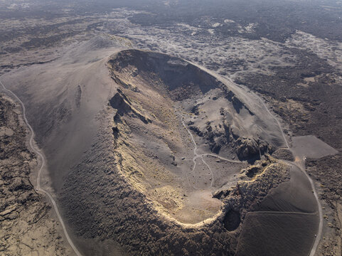 Aerial view of the dramatic volcanic crater with dark rugged terrain and winding paths in Lanzarote, Canarias, Spain.