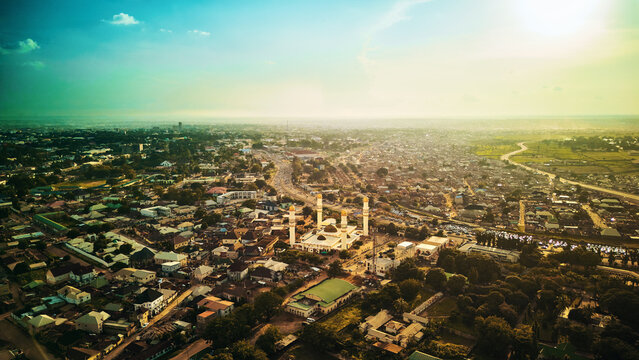 Aerial view of the Sultan Bello Mosque surrounded by dense urban rooftops and greenery under the warm glow of the golden hour in Kaduna, Kaduna, Nigeria.