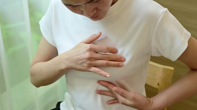 Young Asian woman touching her breast for checking breast size or cancer awareness. Breast self-exam alone is not sufficient to detect breast cancer early.