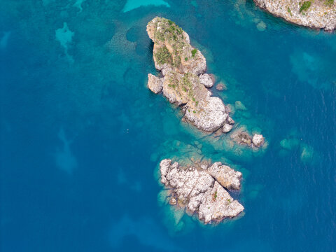 Aerial view of the rocky islets of Riserva Naturale Orientata dello Zingaro surrounded by clear blue sea in San Vito Lo Capo, Sicilia, Italy.
