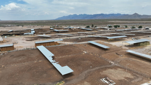 Aerial view of Las Cruces cattle feedlot with rows of metal shelters, dry pens, and distant mountains under a blue sky in Las Cruces, New Mexico, United States.