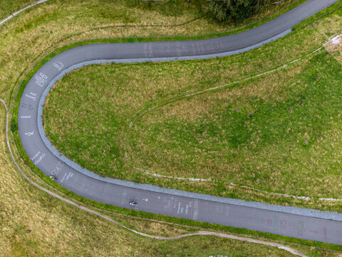 Aerial view of Col du Vam with cyclists riding along the winding asphalt path marked with graffiti, surrounded by green grassy hills in Wijster, Drenthe, Netherlands.