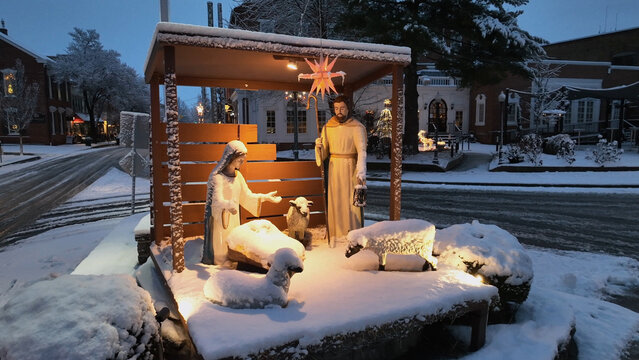 Aerial view of a snow-covered nativity scene with figures of Mary and Joseph surrounded by sheep in a town square at dawn in Lititz, Pennsylvania, United States.