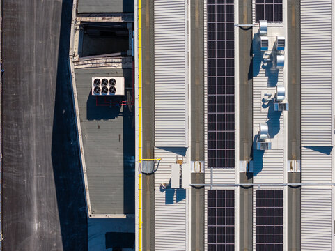 Aerial view of an industrial rooftop featuring rows of solar panels, HVAC ventilation units, and a metal surface adjacent to an asphalt road in Spoleto, Umbria, Italy.