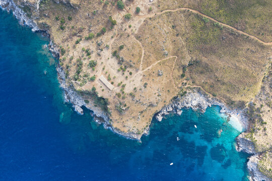 Aerial view of Riserva Naturale Orientata dello Zingaro featuring rugged coastal cliffs, turquoise Mediterranean waters, hiking trails, and small boats in San Vito Lo Capo, Sicilia, Italy.