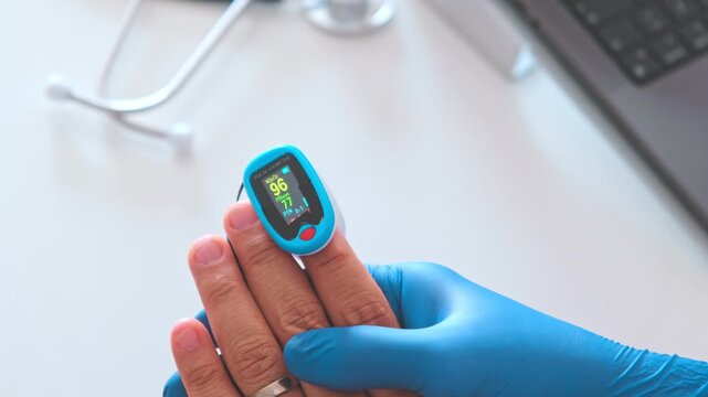 Doctor in blue gloves checking patient's blood oxygen level with a modern pulse oximeter device