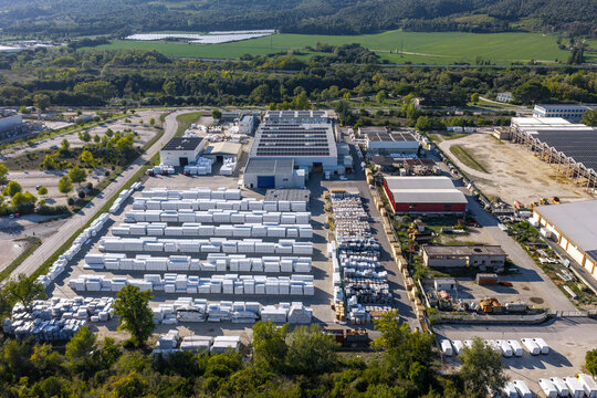 Aerial view of an industrial facility with rows of white packaged goods in storage, solar panel rooftops, and surrounding green landscape in Nera Montoro, Umbria, Italy.