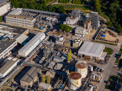 Aerial view of an industrial complex featuring large storage tanks, interconnected piping systems, and factory buildings surrounded by lush green trees in Nera Montoro, Umbria, Italy.