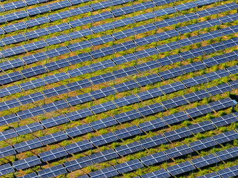 Aerial view of a large industrial solar farm with rows of photovoltaic panels installed in a grassy field in Nera Montoro, Umbria, Italy.