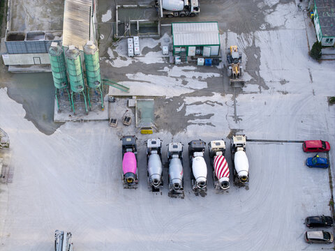 Aerial view of a concrete batching plant featuring several cement mixer trucks parked in a row, industrial silos, and construction equipment in Krakow, Lesser Poland Voivode, Poland.