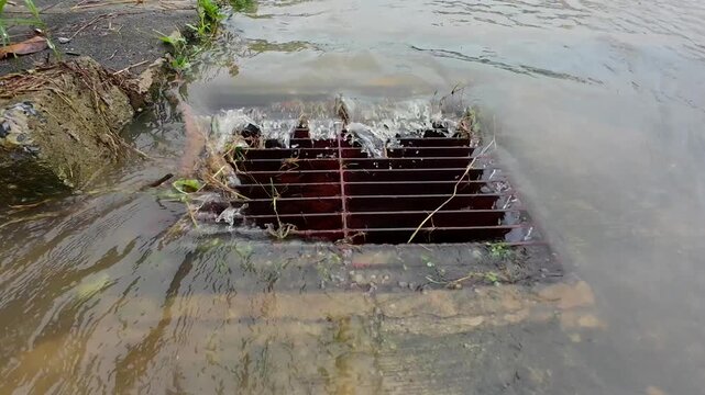 Water during a rainstorm flows into the drainage grate. Rainwater flowing down the impervious pavement to the storm drain equipped with cast iron grid during a rain