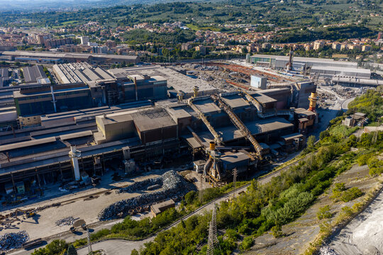 Aerial view of Acciai Speciali Terni S.p.A. steel plant with large industrial buildings, metal scrap piles, and surrounding greenery in Terni, Umbria, Italy.