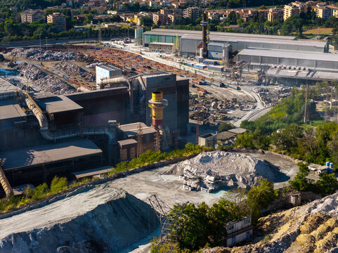 Aerial view of Acciai Speciali Terni S.p.A. steelworks facility with industrial buildings, large piles of scrap metal, and railway tracks in Terni, Umbria, Italy.