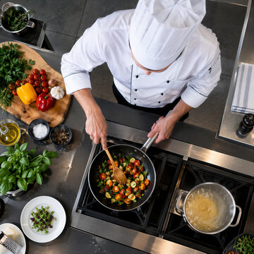 Top view of professional male chef in uniform cooking fresh vegetables and pasta in modern commercial kitchen
