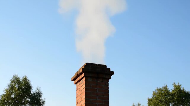Smoke from a red brick chimney, close-up of a blue sky chimney