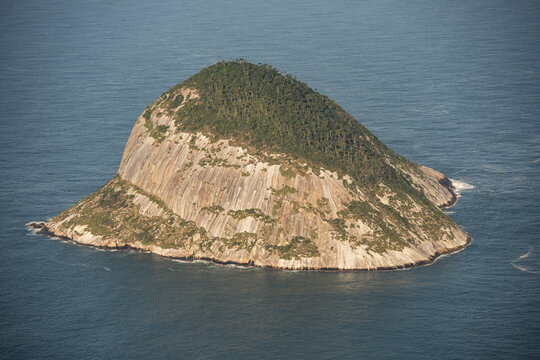 Aerial view of the rocky island of Ilha Rasa rising from the deep blue Atlantic Ocean with steep granite cliffs and lush green vegetation in Rio de Janeiro, Rio de Janeiro, Brazil.