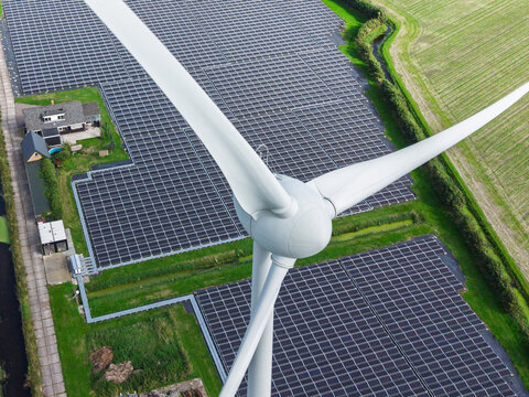 Aerial view of a large solar farm and a wind turbine in a rural landscape with green fields and a small house in 't Zand, North Holland, Netherlands.