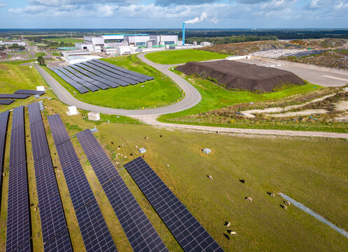 Aerial view of a solar park integrated with a waste management facility, featuring rows of solar panels on green fields with grazing sheep in Wijster, Drenthe, Netherlands.